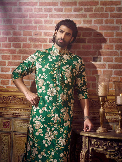 Man wearing a green floral kurta against a brick wall.