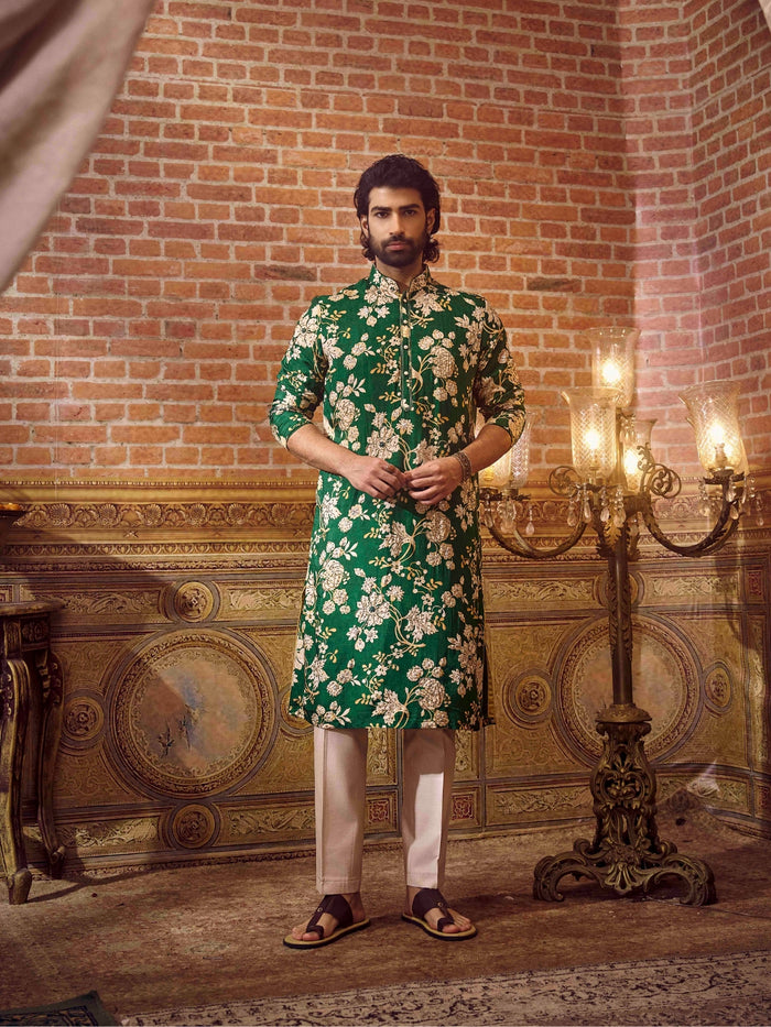 Man wearing a green floral kurta with white pants in an ornate room.