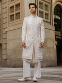 Man wearing a traditional white sherwani standing in front of an architectural building.