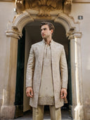 Man wearing a traditional embroidered sherwani standing in front of an ornate archway.