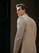 Man wearing a beige embroidered sherwani against a dark background