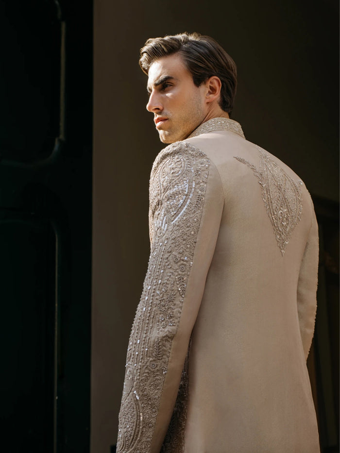 Man wearing a beige embroidered sherwani against a dark background