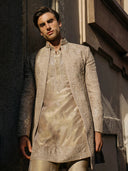 Man wearing a traditional embroidered sherwani against a textured wall.