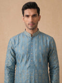 Man wearing a blue embroidered kurta against a beige background