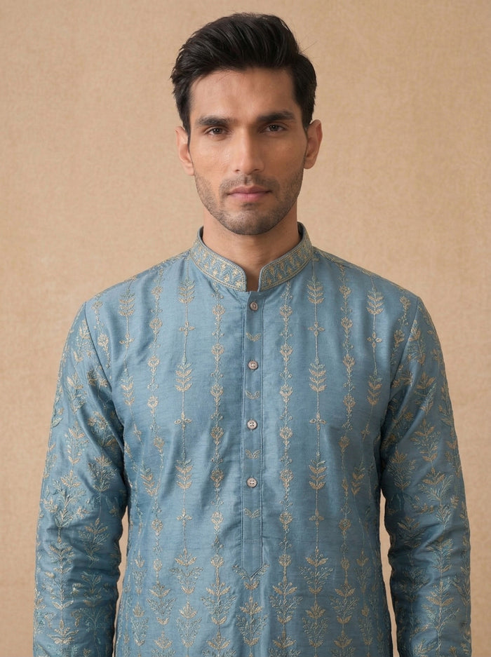 Man wearing a blue embroidered kurta against a beige background