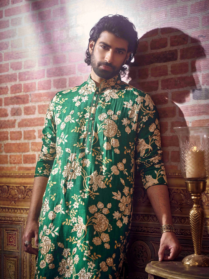 Man wearing a green floral kurta against a brick wall.