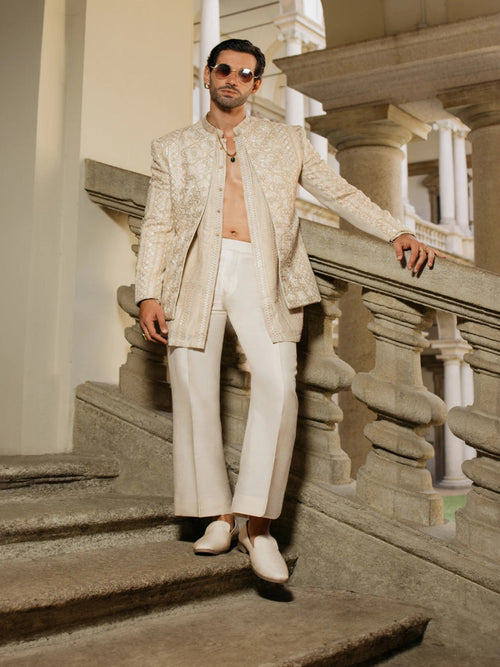 Man in a beige indowestern standing on stone steps with classical architecture in the background