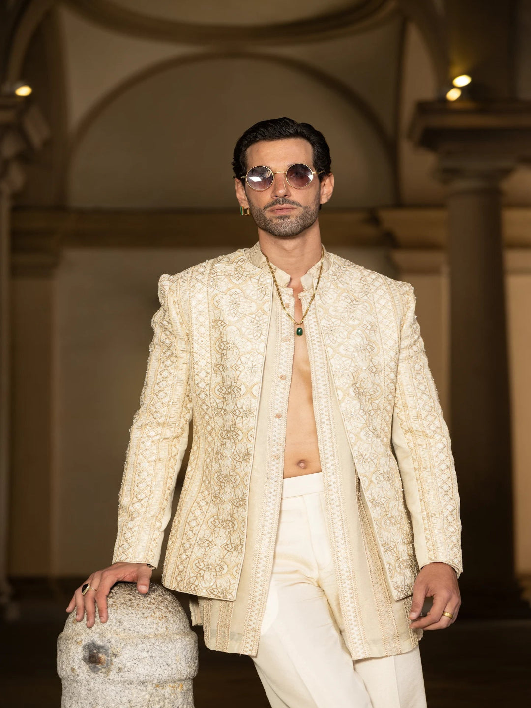 Man wearing a cream embroidered blazer and sunglasses in an indoor setting