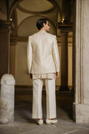 Man in a cream-colored suit standing in an archway with stone columns.