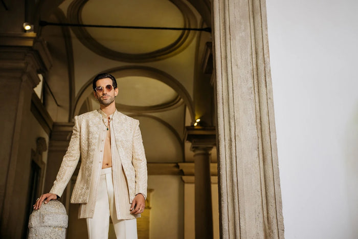 Man in a beige suit standing in an architectural setting with columns.